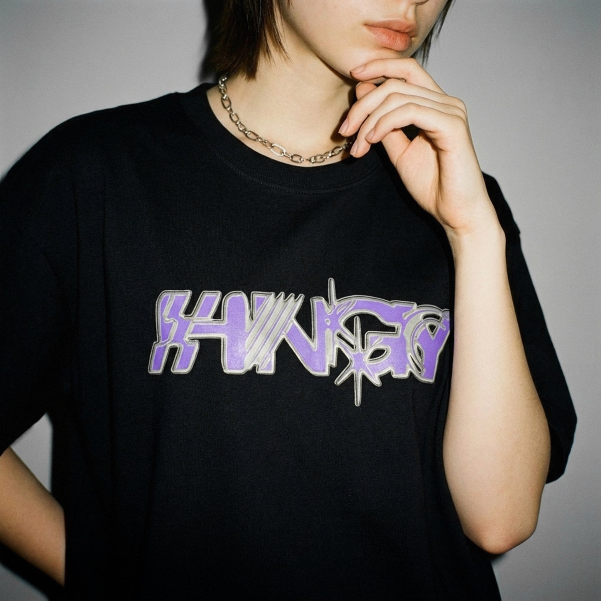 Close-up of the purple graffiti HNGY logo on the oversized black t-shirt
